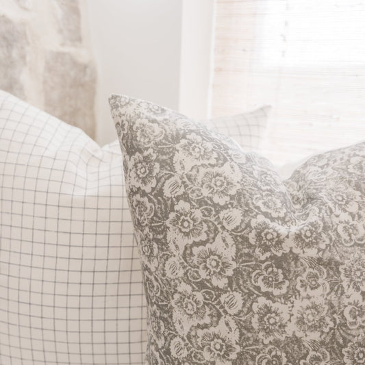 Gray and cream floral patterned pillow with coordinating grid-patterned pillow beside it.