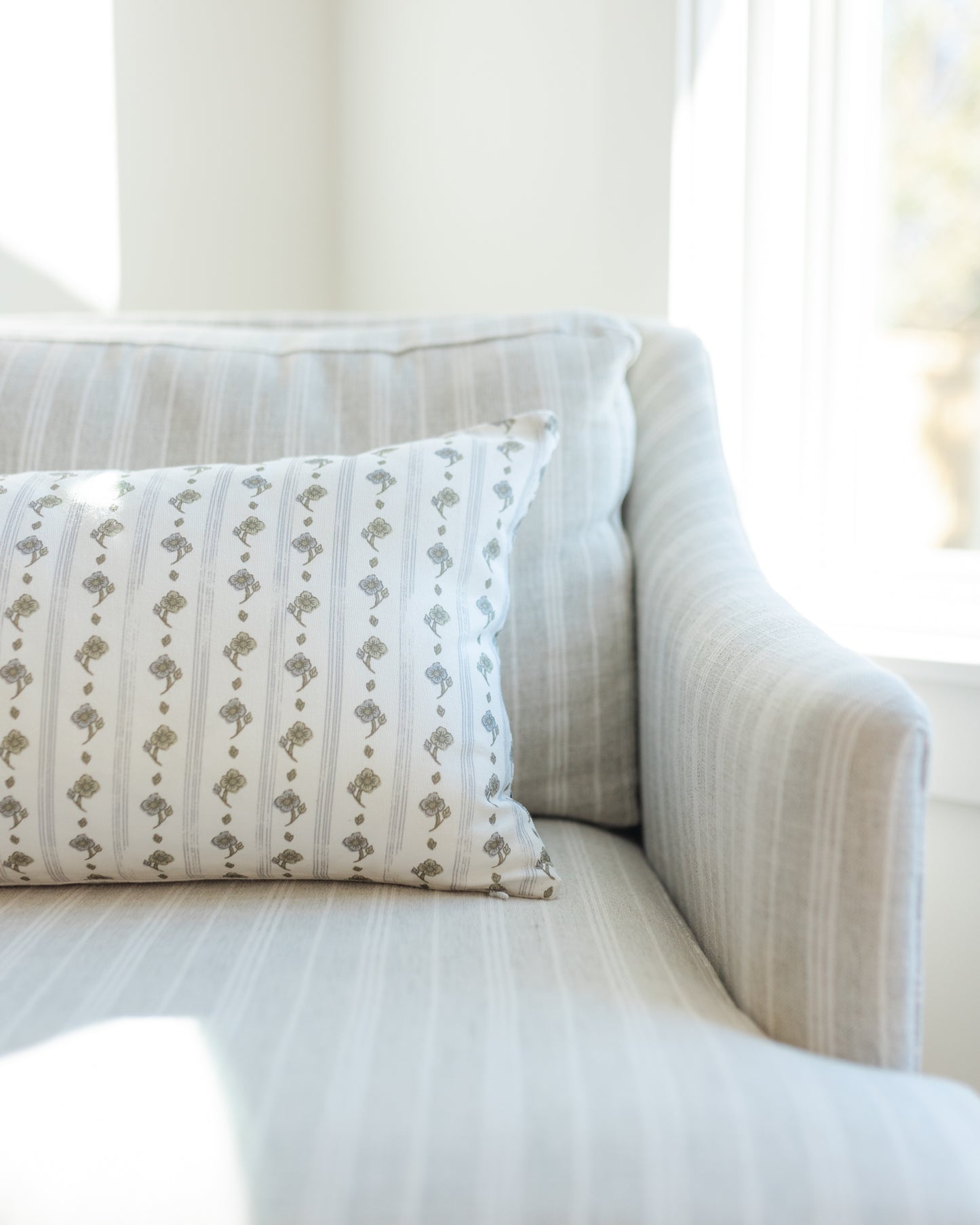 Lumbar pillow with sage green floral stripe pattern on white background, placed on light striped upholstered chair.