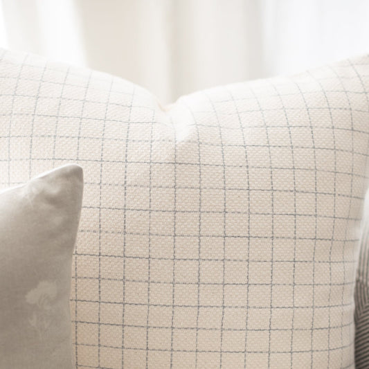 Cream-colored pillow with gray grid pattern and white piping detail.