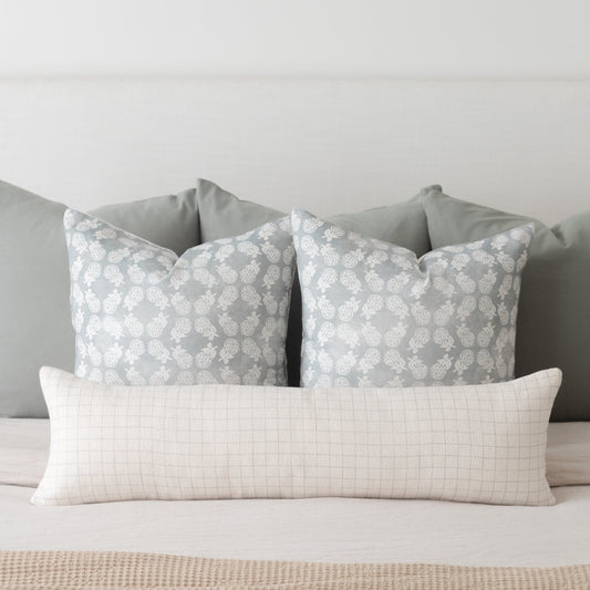 Cream-colored lumbar pillow with fine grid pattern, displayed with two gray patterned pillows on a bed.