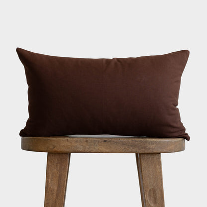 Dark brown rectangular pillow placed on a wooden stool against a light gray background.
