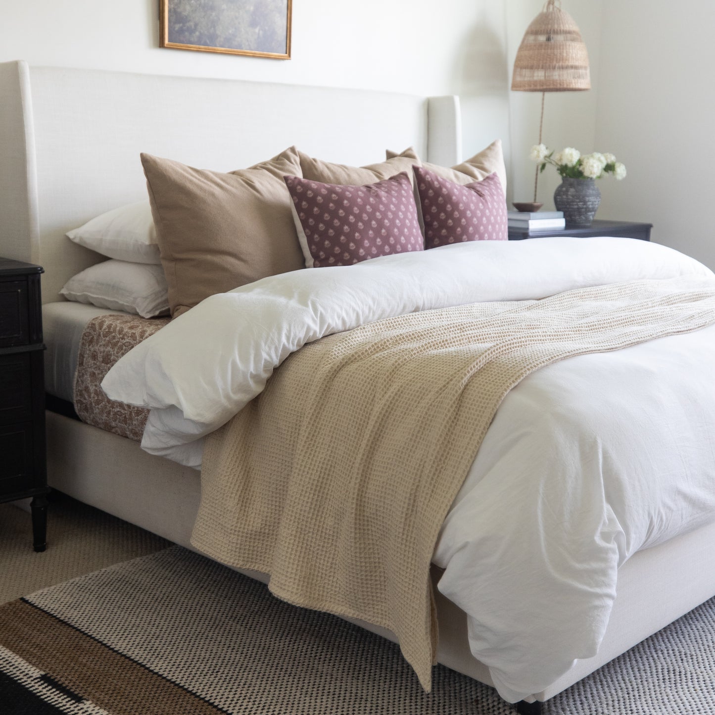 Ivory waffle-textured blanket draped across a bed with white bedding and decorative pillows.