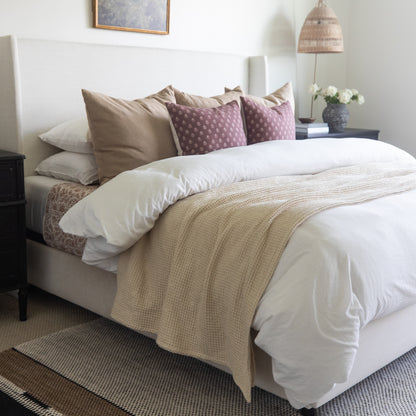 Ivory waffle-textured blanket draped across a bed with white bedding and decorative pillows.