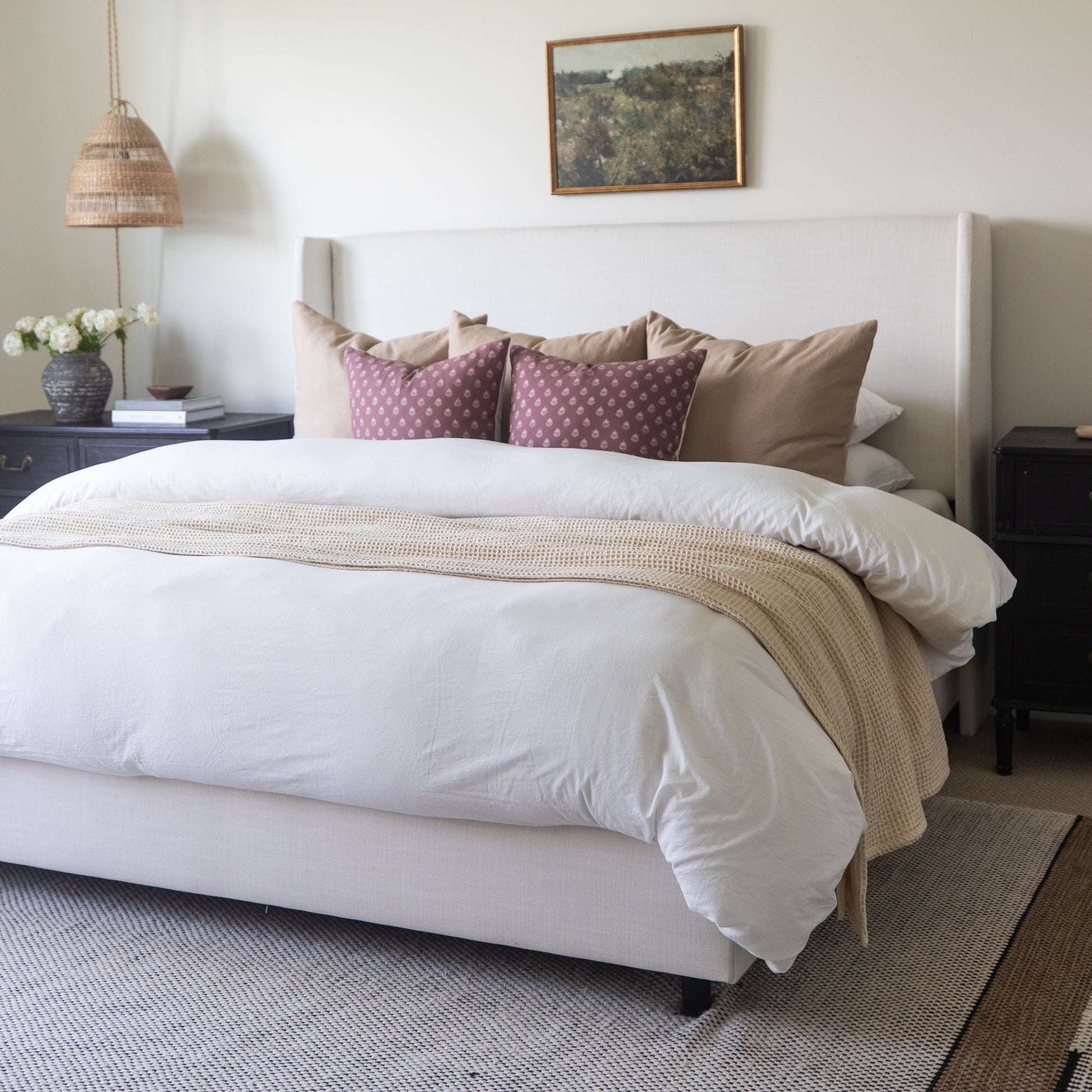 Ivory waffle-textured blanket draped over a bed with white bedding and decorative pillows.