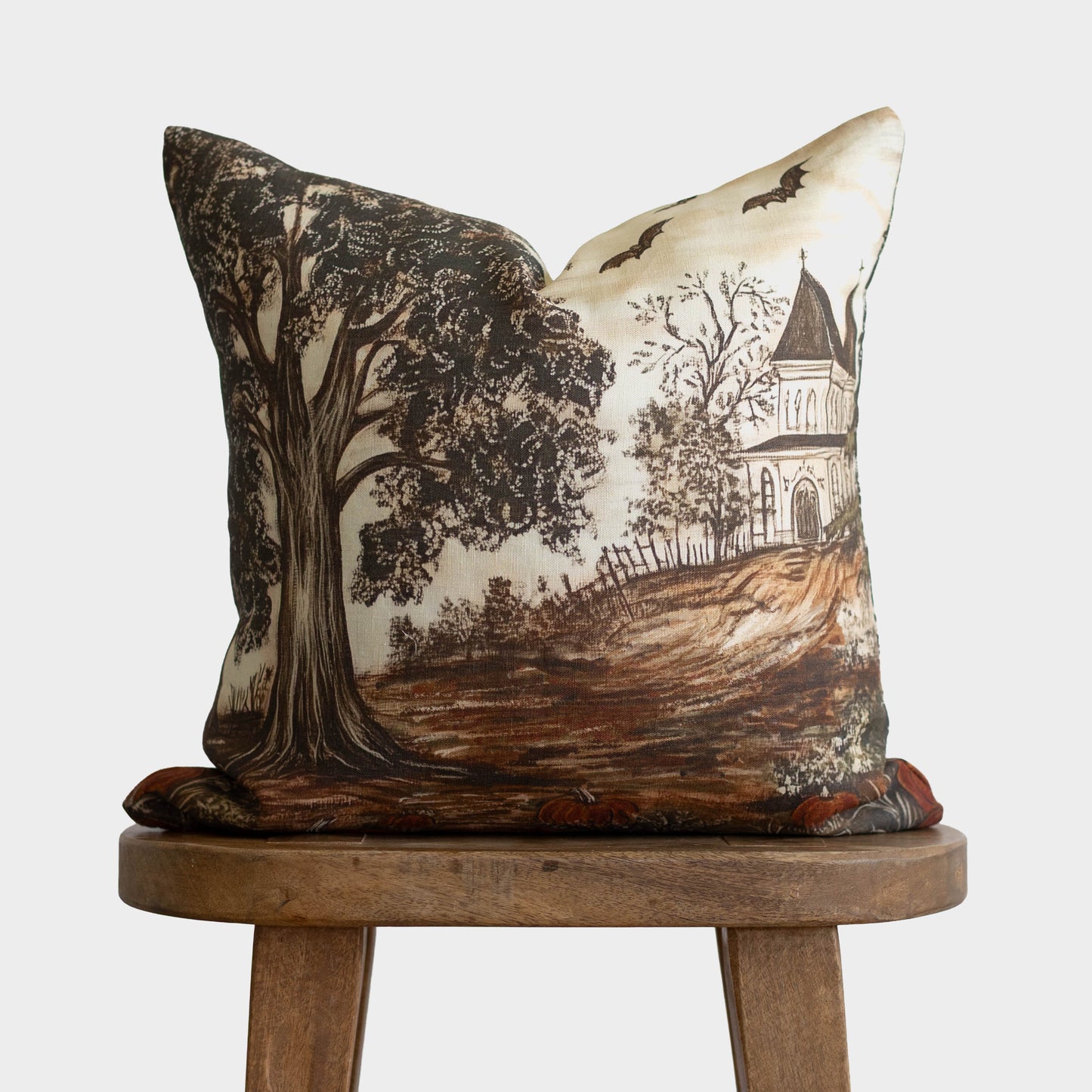 Linen pillow with haunted house, gnarled tree, and flying bats in black and brown on cream background.
