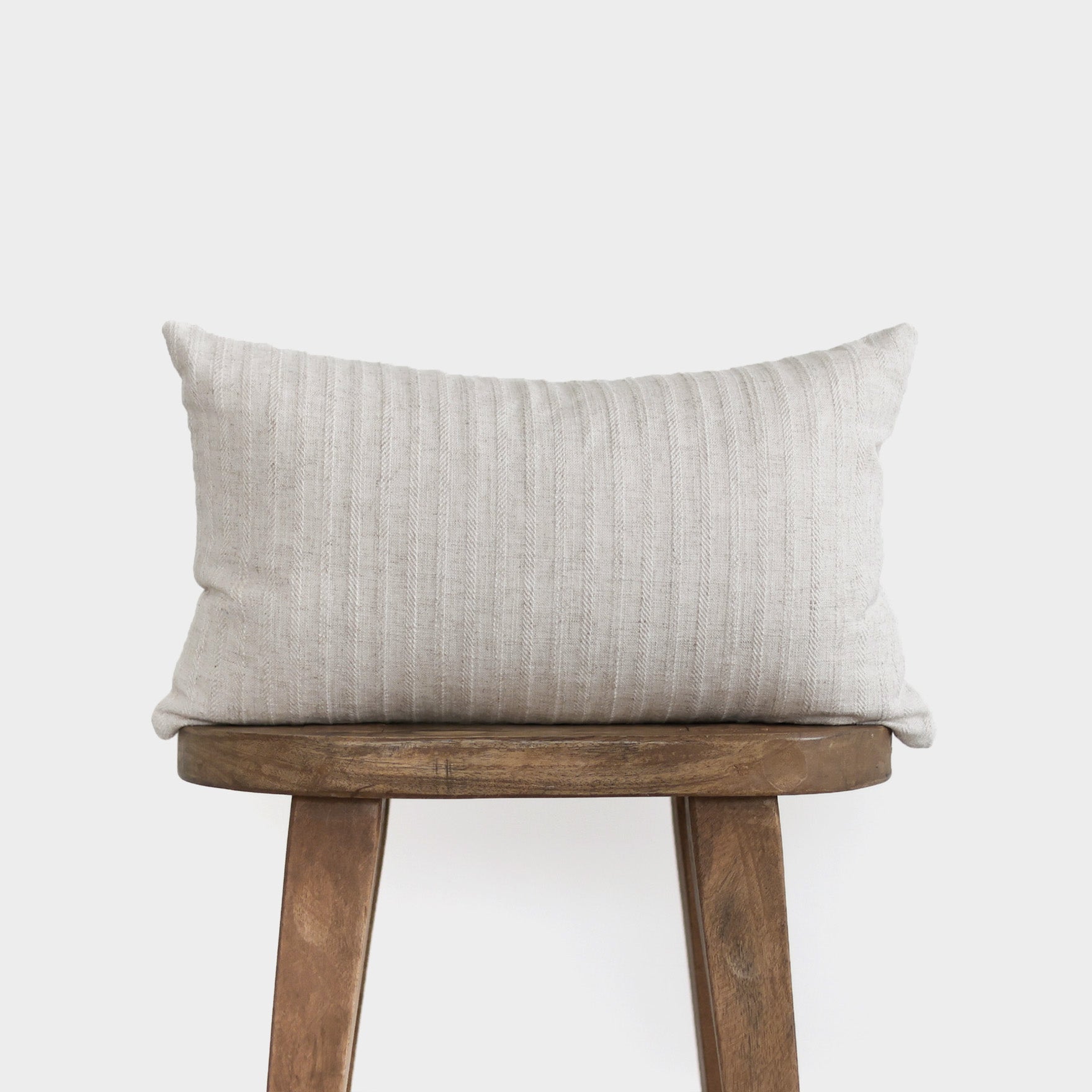 Cream ribbed rectangular pillow with vertical texture on wooden stool.