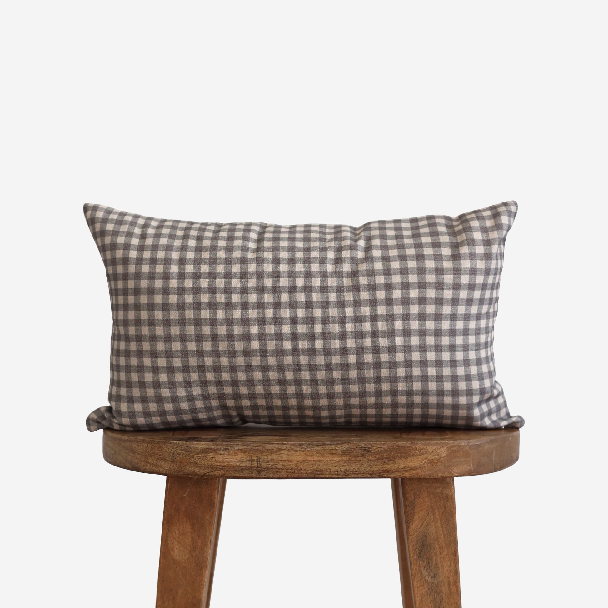 Brown and white gingham patterned lumbar pillow displayed on a wooden stool.