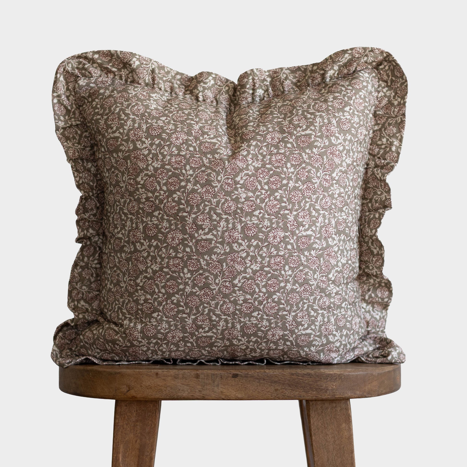 Taupe and cream floral patterned pillow with ruffled edges on wooden stool.