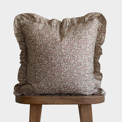 Taupe and cream floral patterned pillow with ruffled edges on wooden stool.