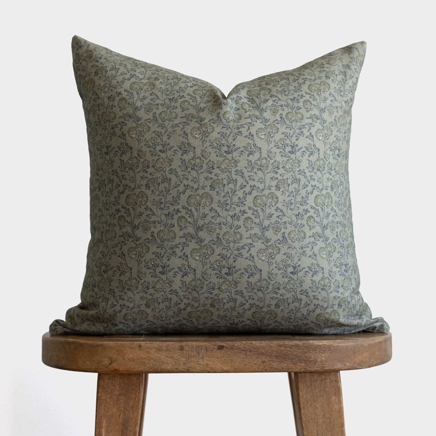 Green damask patterned pillow displayed on wooden stool against white background.