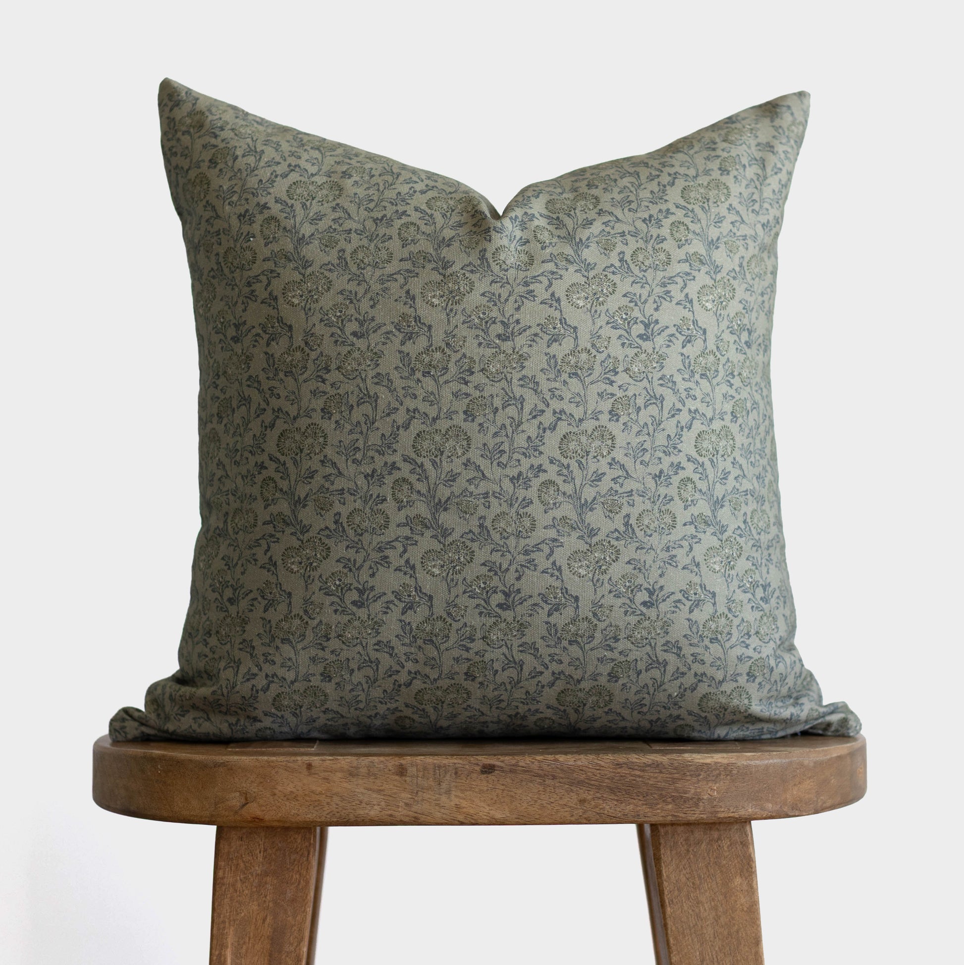 Green damask patterned pillow displayed on wooden stool against white background.
