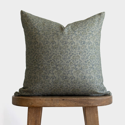 Green damask patterned pillow displayed on wooden stool against white background.