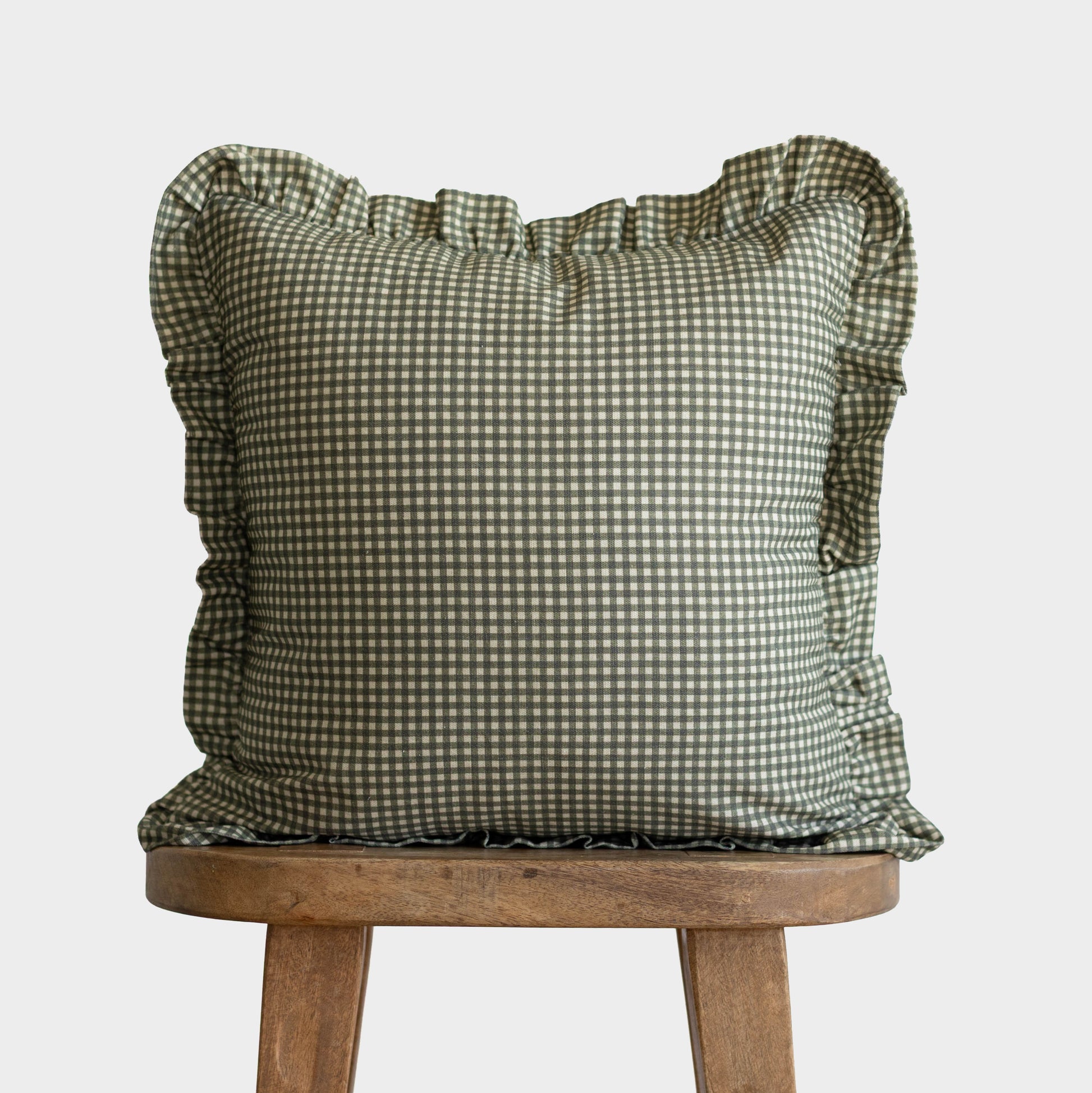 Green and white mini gingham pillow with ruffled edges on all sides, displayed on a wooden stool.