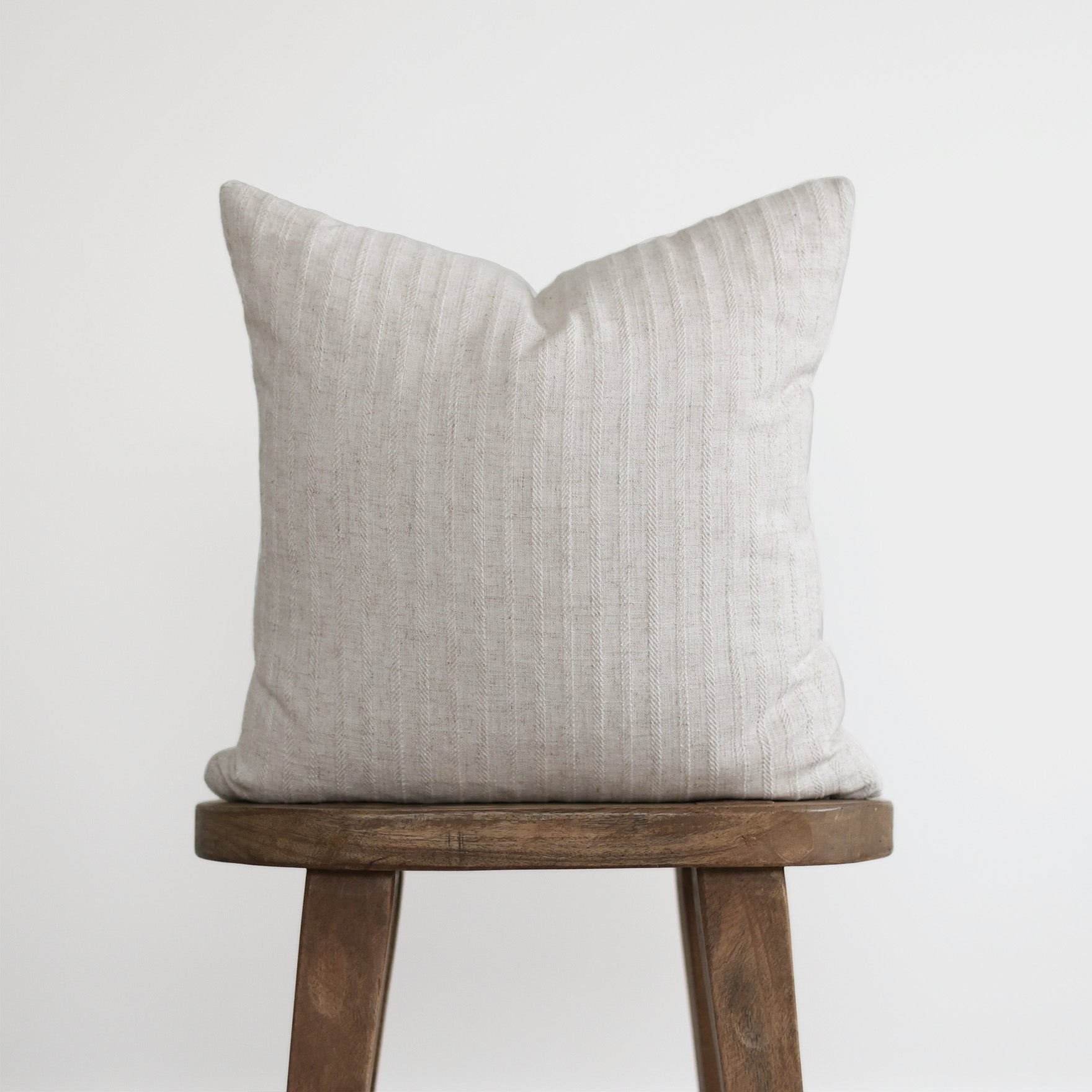 Cream textured linen pillow with vertical striping, displayed on a wooden stool.