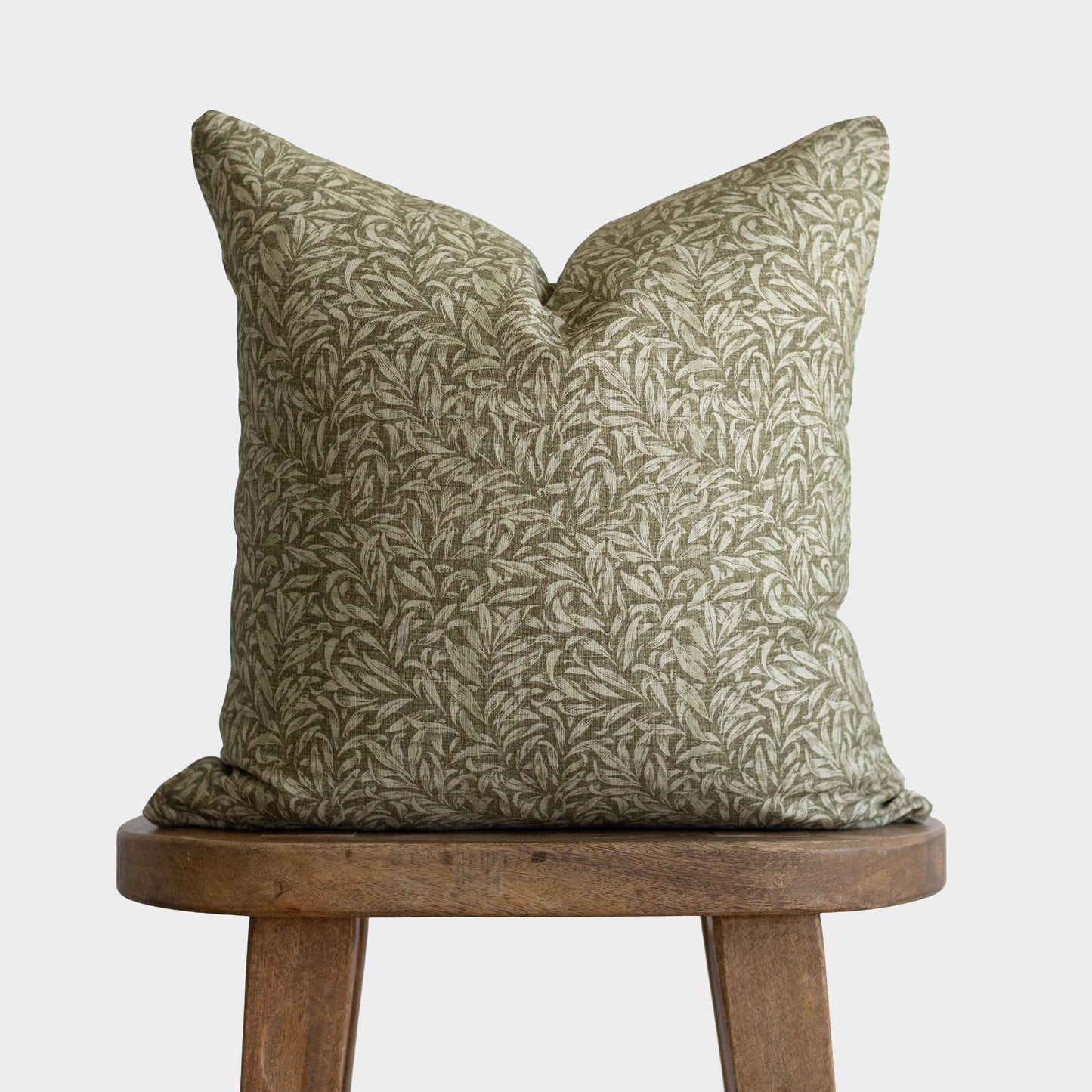 Green and cream botanical patterned pillow with envelope closure on wooden stool.