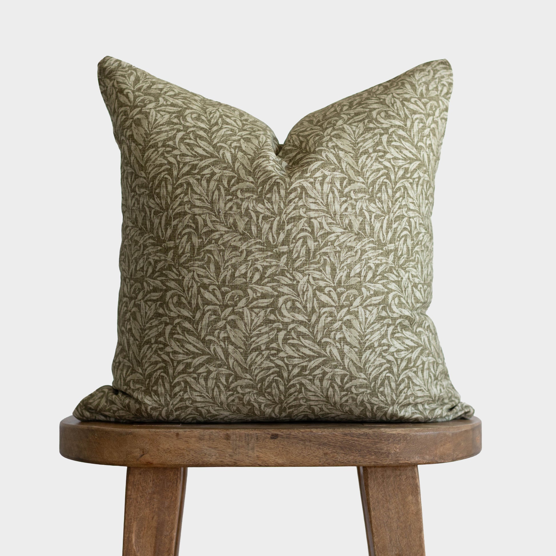 Green and cream botanical patterned pillow with envelope closure on wooden stool.