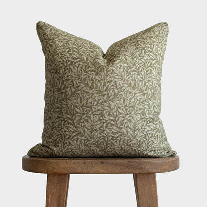 Green and cream botanical patterned pillow with envelope closure on wooden stool.