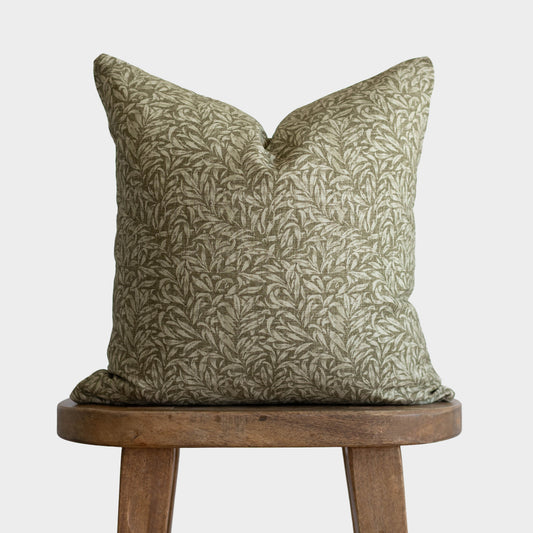 Green and cream botanical patterned pillow with envelope closure on wooden stool.