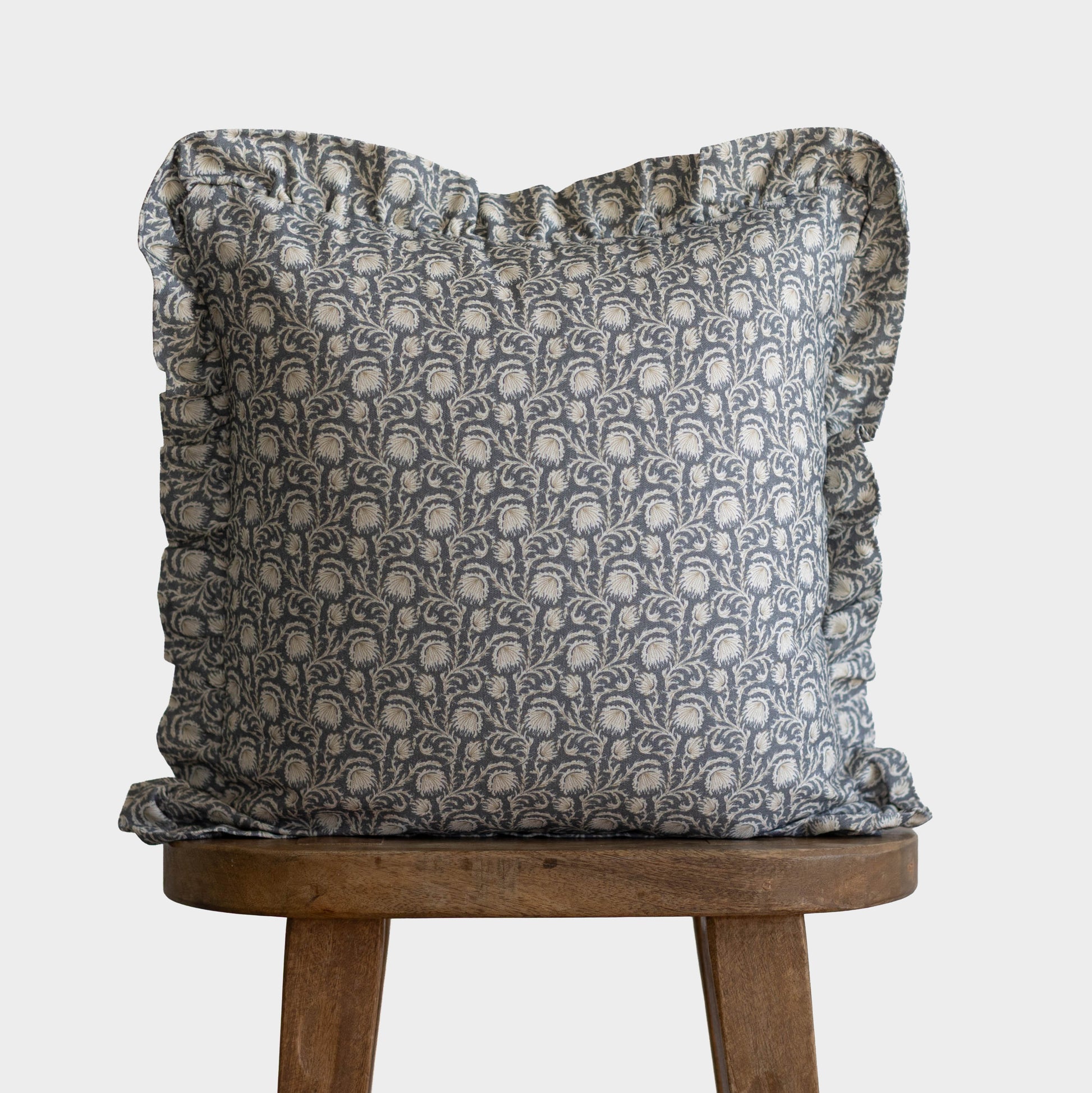 Gray and cream damask patterned pillow with ruffled edges on wooden stool.