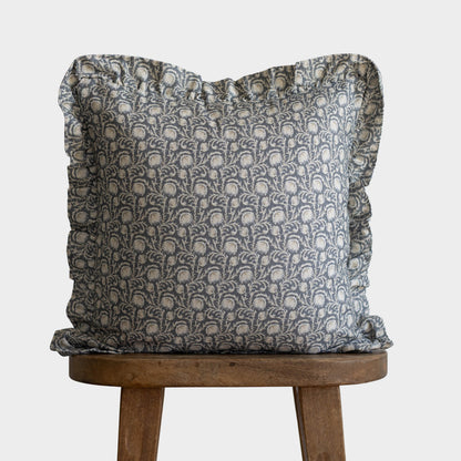 Gray and cream damask patterned pillow with ruffled edges on wooden stool.