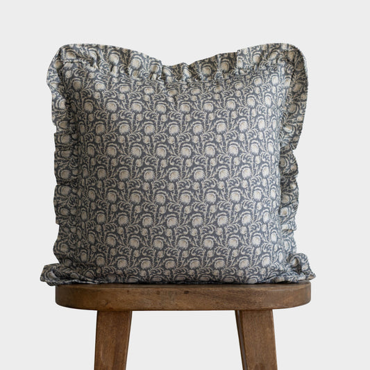 Gray and cream damask patterned pillow with ruffled edges on wooden stool.