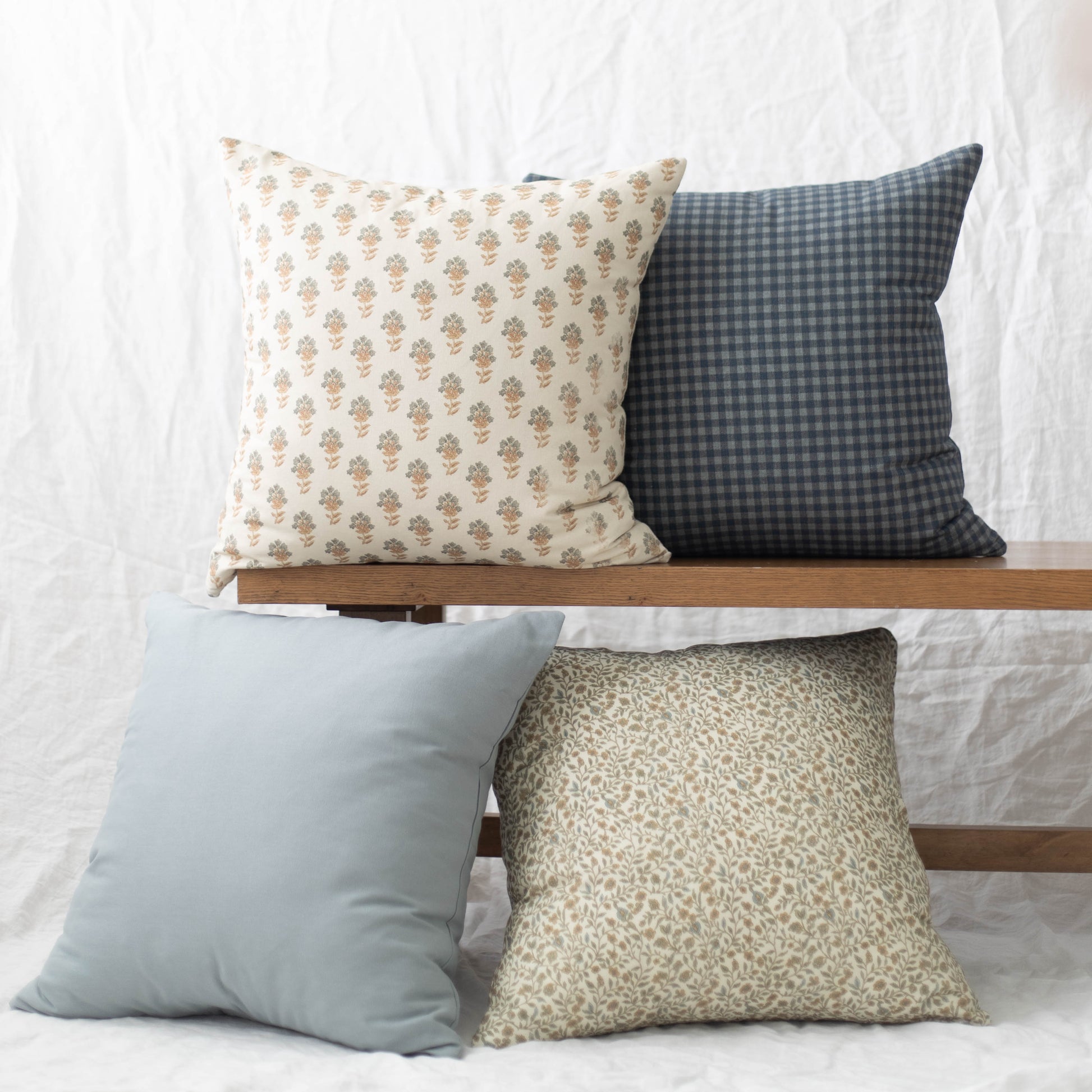 Four Cove pillows in varying sizes and patterns: floral print, gingham check, solid light blue, and textured neutral design.