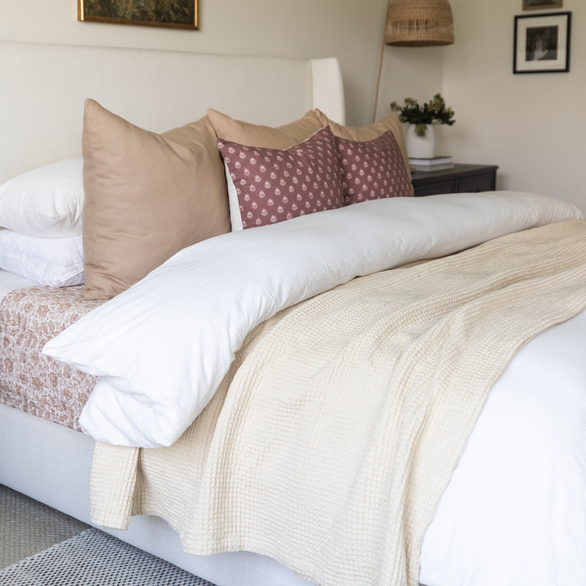 Ivory waffle-weave blanket draped across a bed with white pillows and decorative cushions.