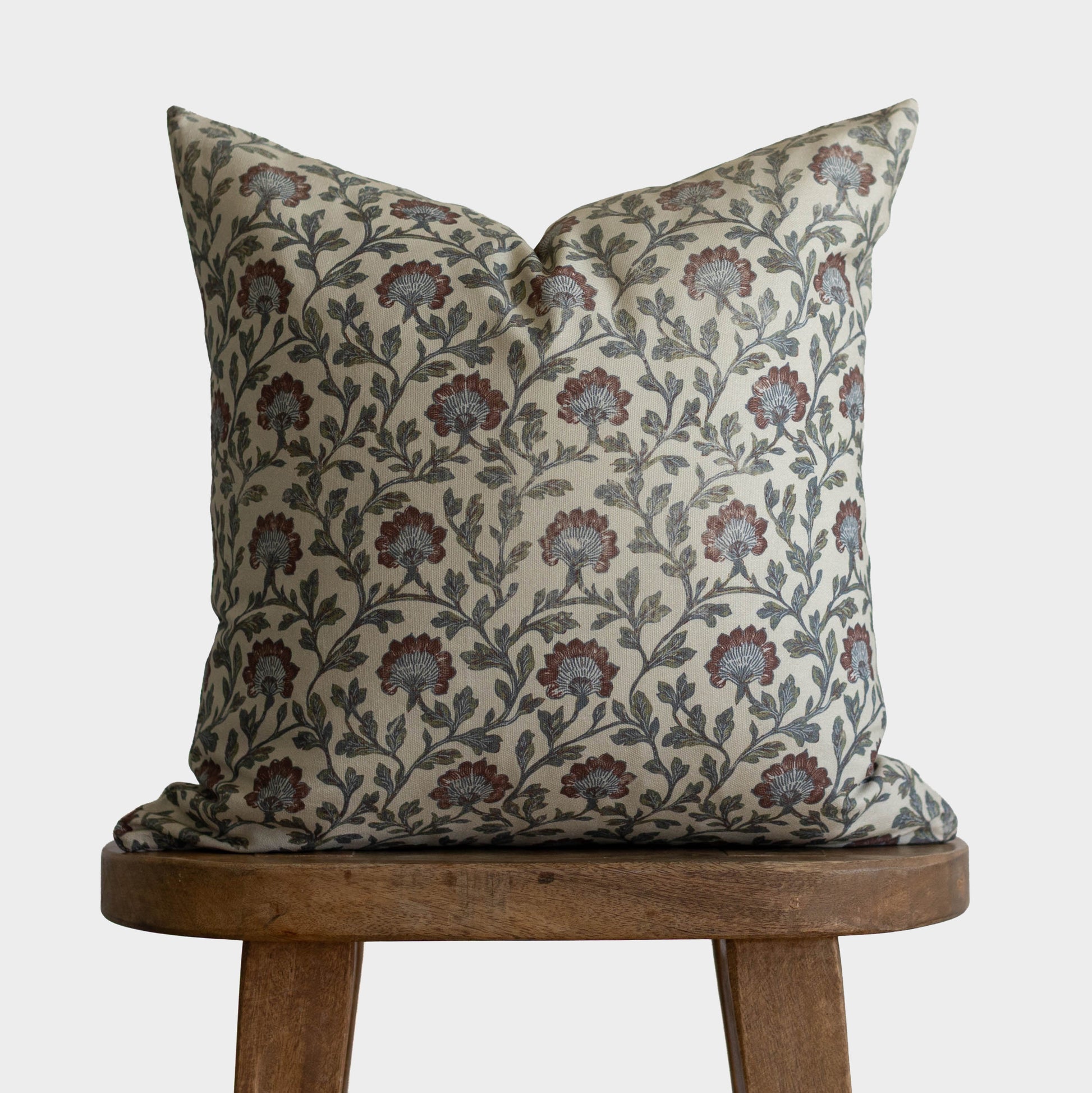 Multicolor floral patterned pillow with red and blue flowers on cream background, displayed on wooden stool.