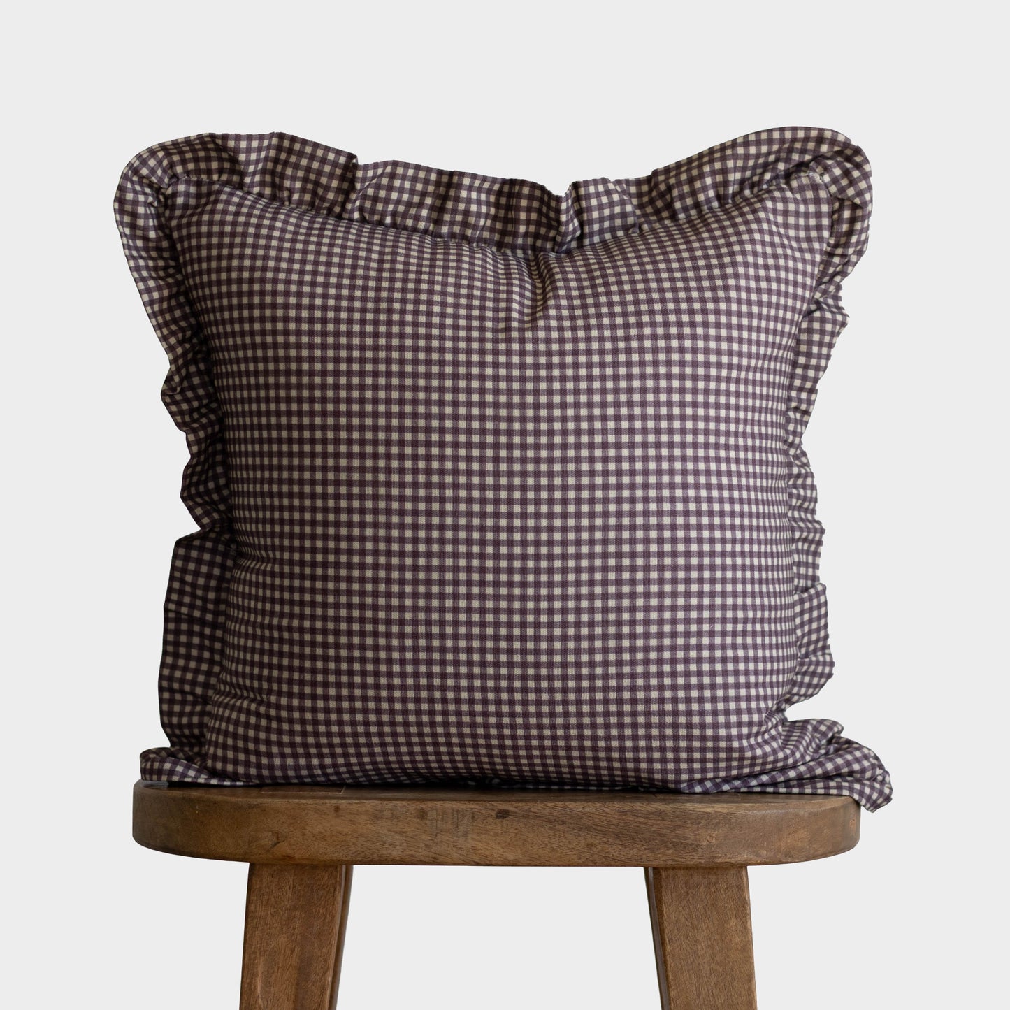 Plum and white gingham square pillow with ruffled edges on wooden stool.