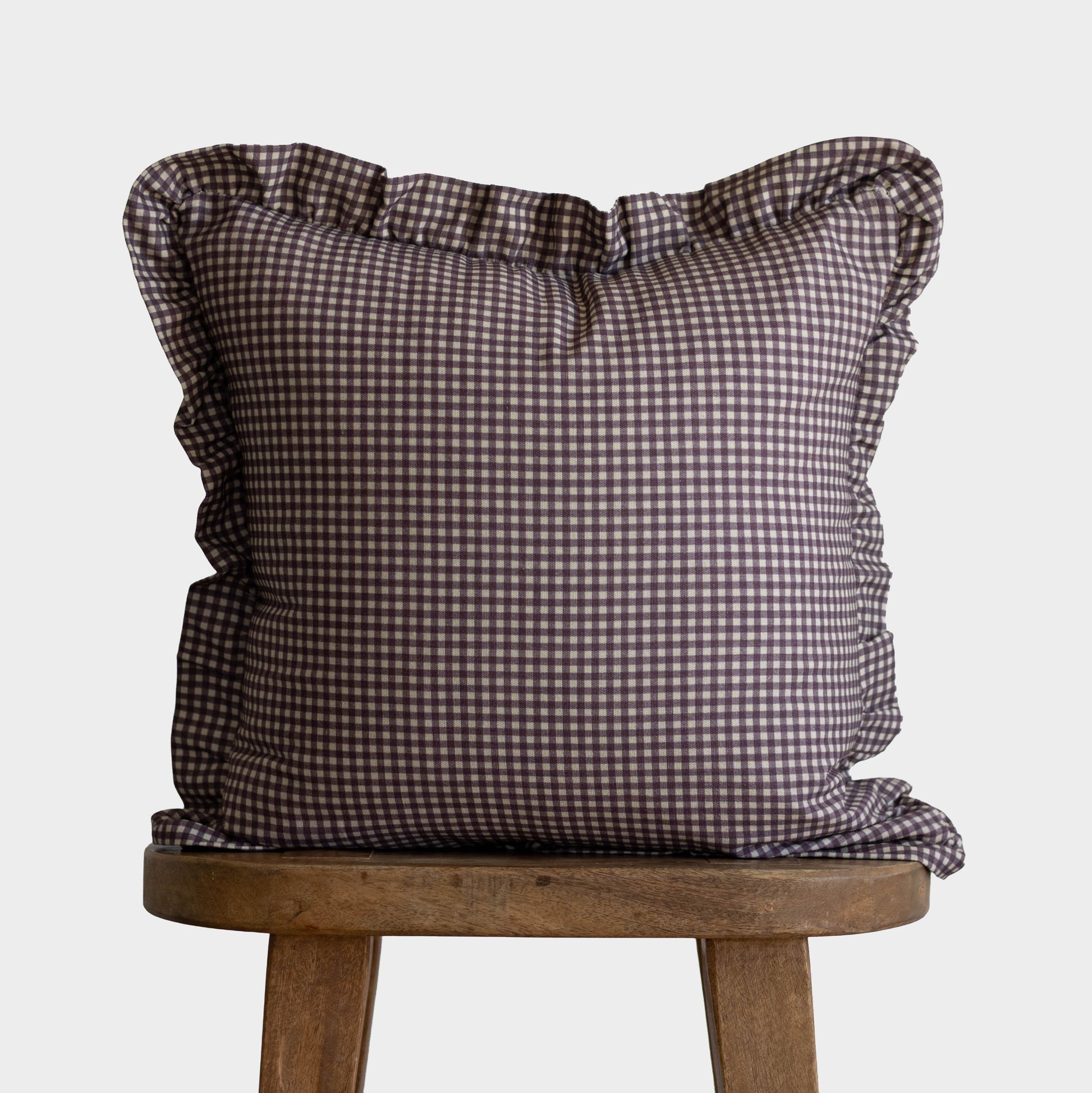 Plum and white gingham square pillow with ruffled edges on wooden stool.