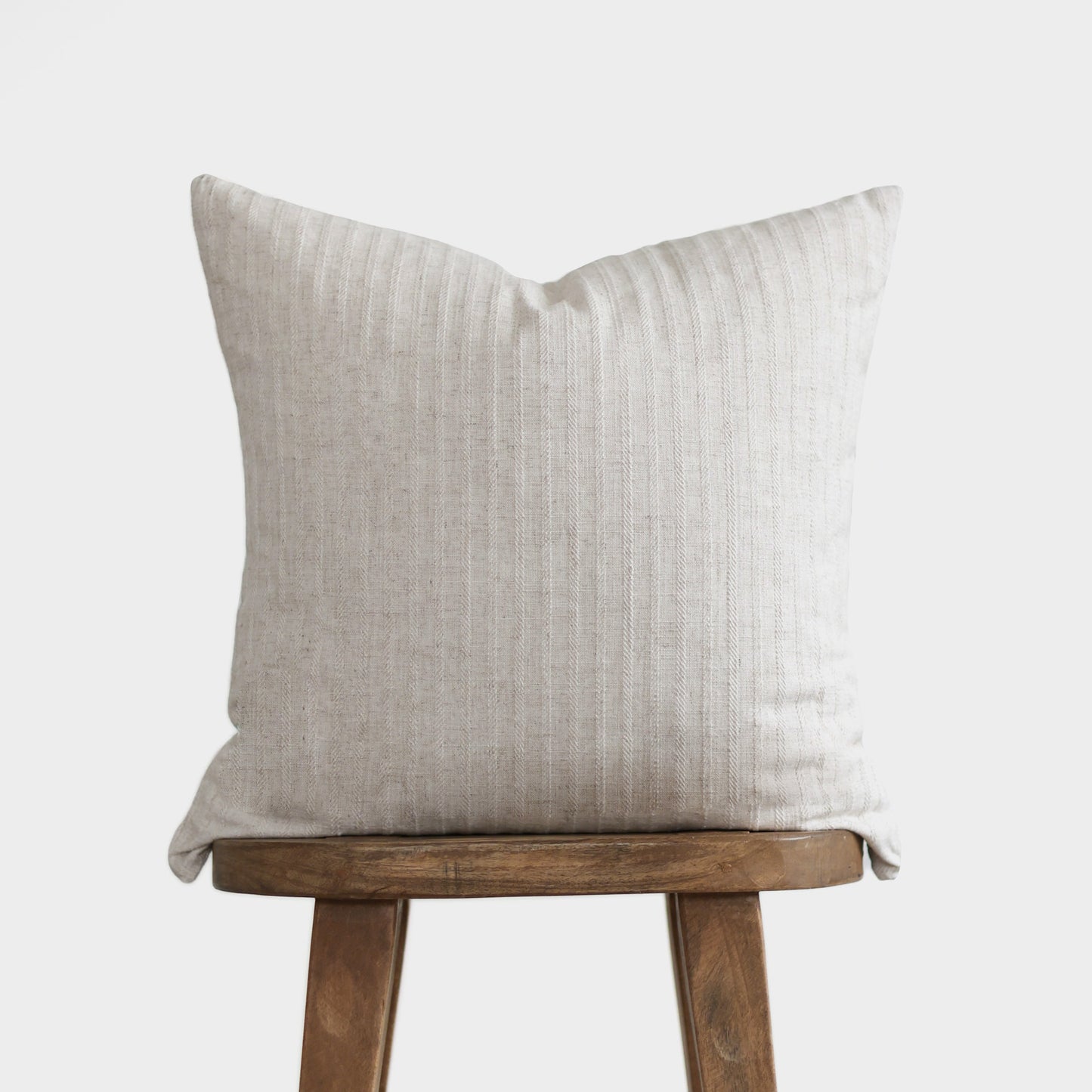 Cream linen pillow with vertical ribbed texture on wooden stool.
