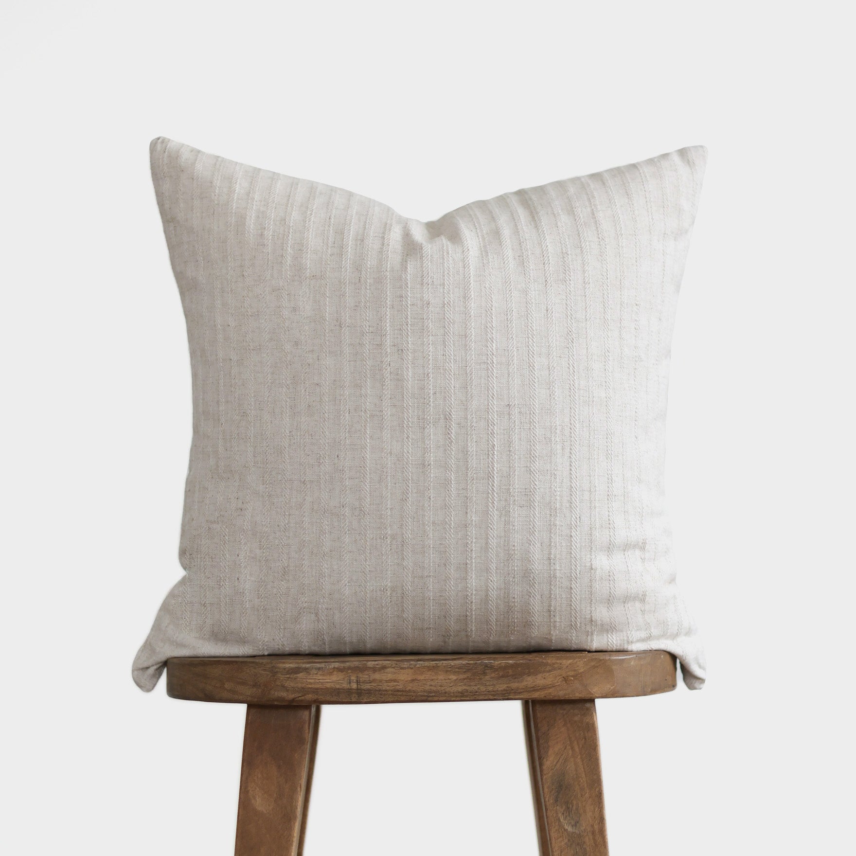 Cream linen pillow with vertical ribbed texture on wooden stool.