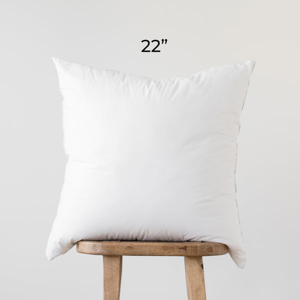 White square faux down pillow insert, 22 inches, displayed on wooden stand.