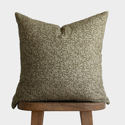 Green and cream damask patterned throw pillow displayed on wooden stool.