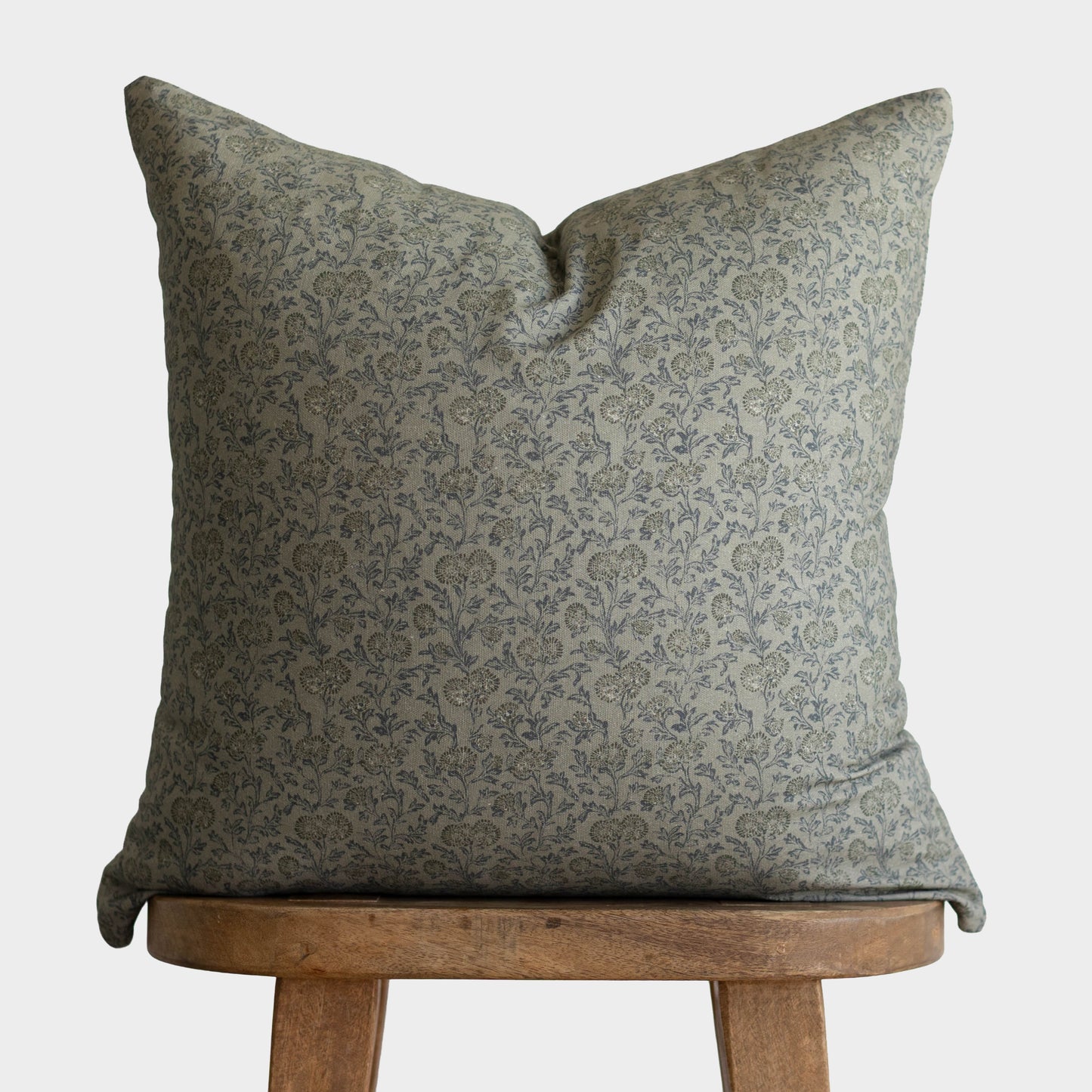 Green damask patterned pillow with envelope closure displayed on wooden stool.