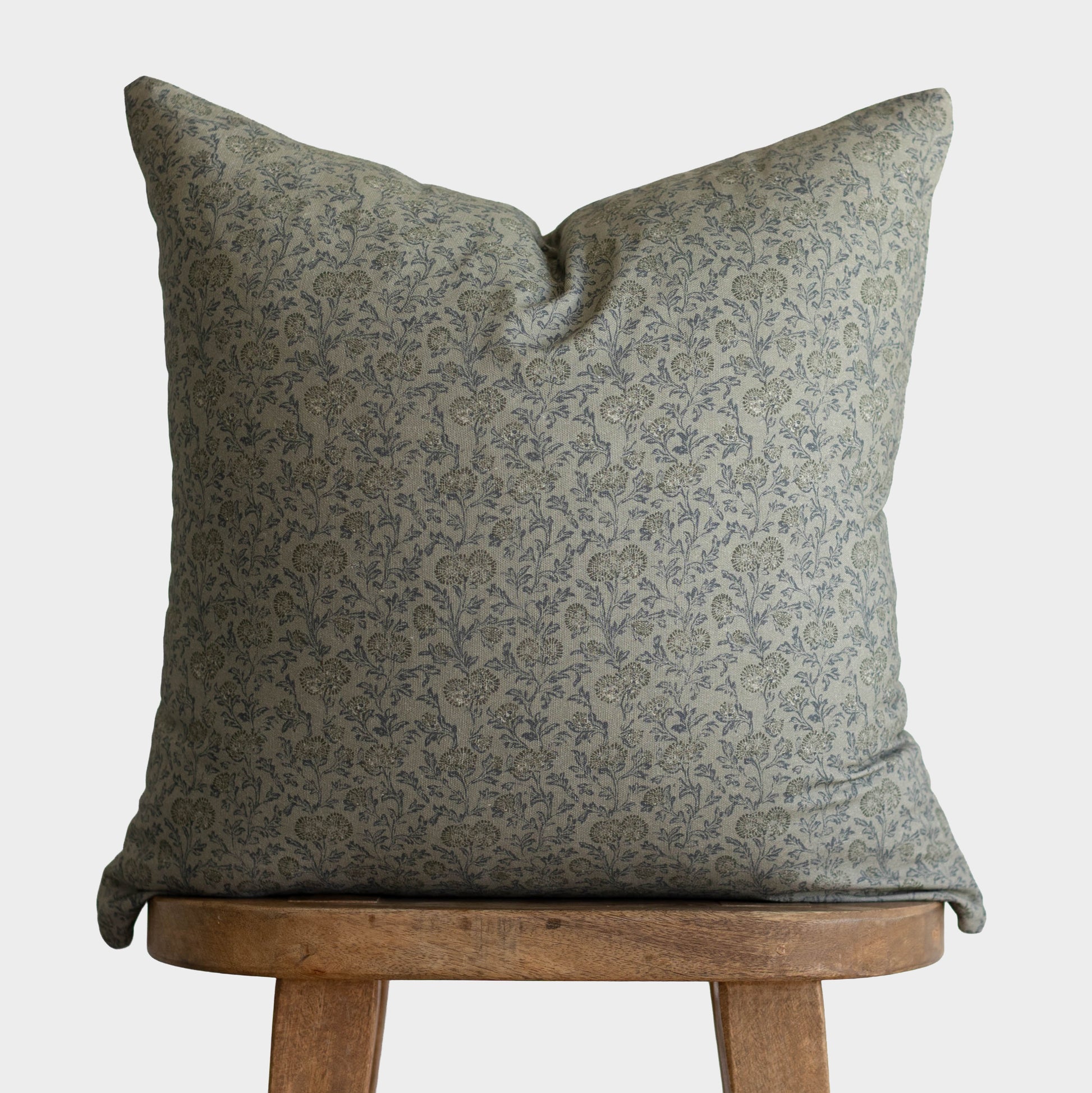 Green damask patterned pillow with envelope closure displayed on wooden stool.