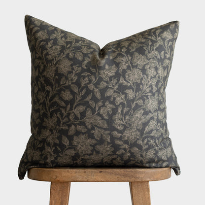 Charcoal gray and gold botanical damask pillow on wooden chair back.