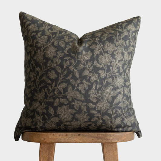 Charcoal gray and gold botanical damask pillow on wooden chair back.