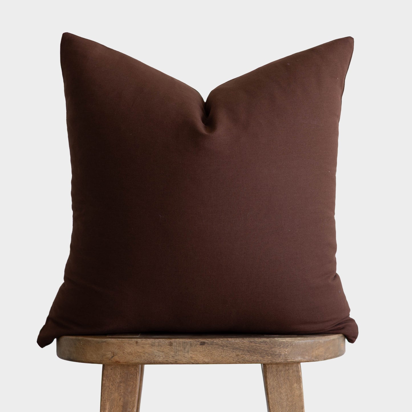 Dark brown linen pillow cover with envelope closure displayed on wooden stool.