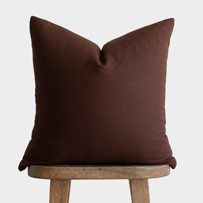 Dark brown linen pillow cover with envelope closure displayed on wooden stool.