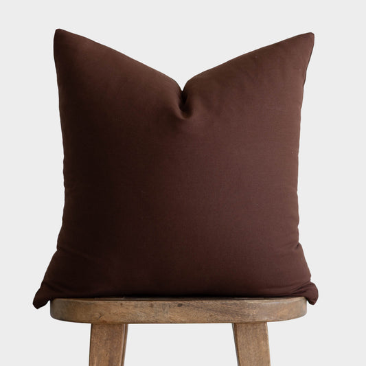 Dark brown linen pillow cover with envelope closure displayed on wooden stool.