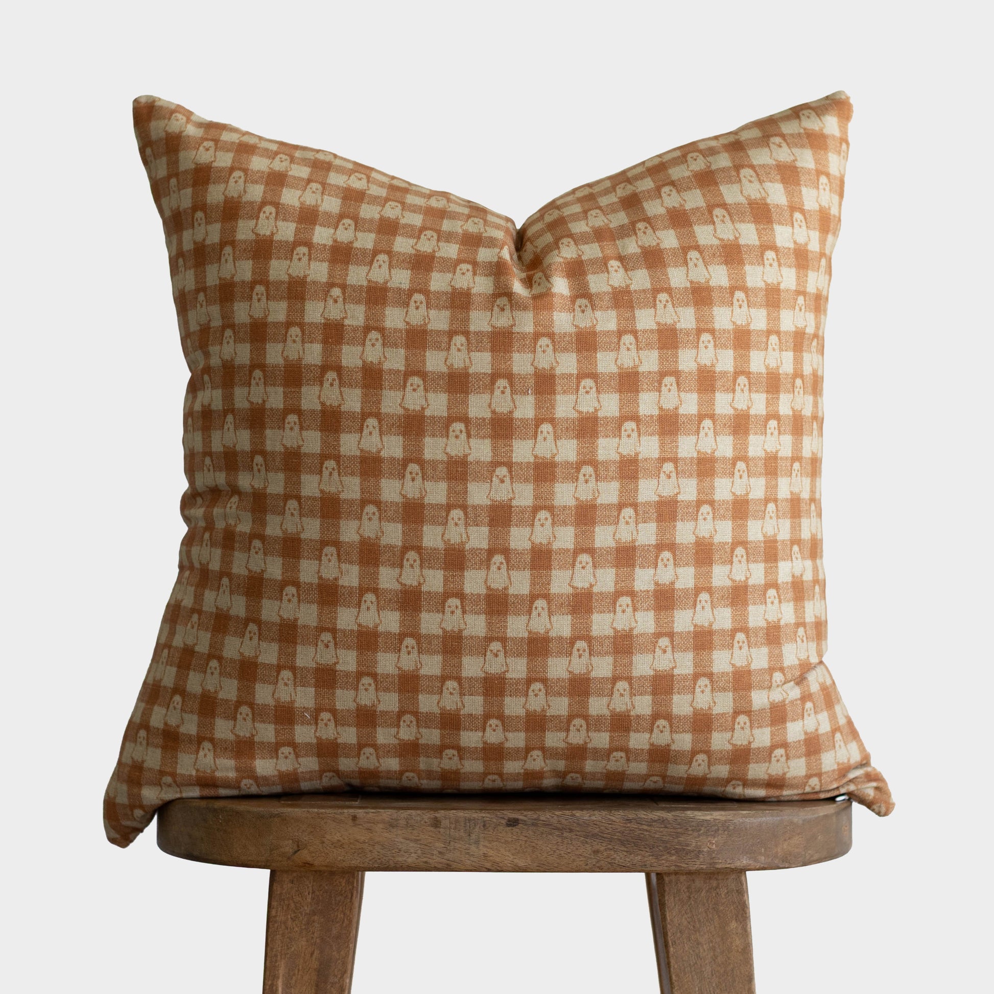 Tan and cream gingham pillow with ghost motifs displayed on wooden stool.