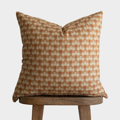 Tan and cream gingham pillow with ghost motifs displayed on wooden stool.