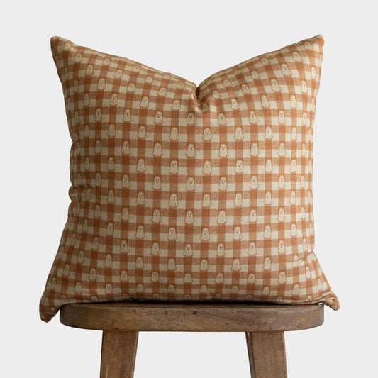 Orange and cream checkered pillow with small geometric pattern, displayed on wooden stool.