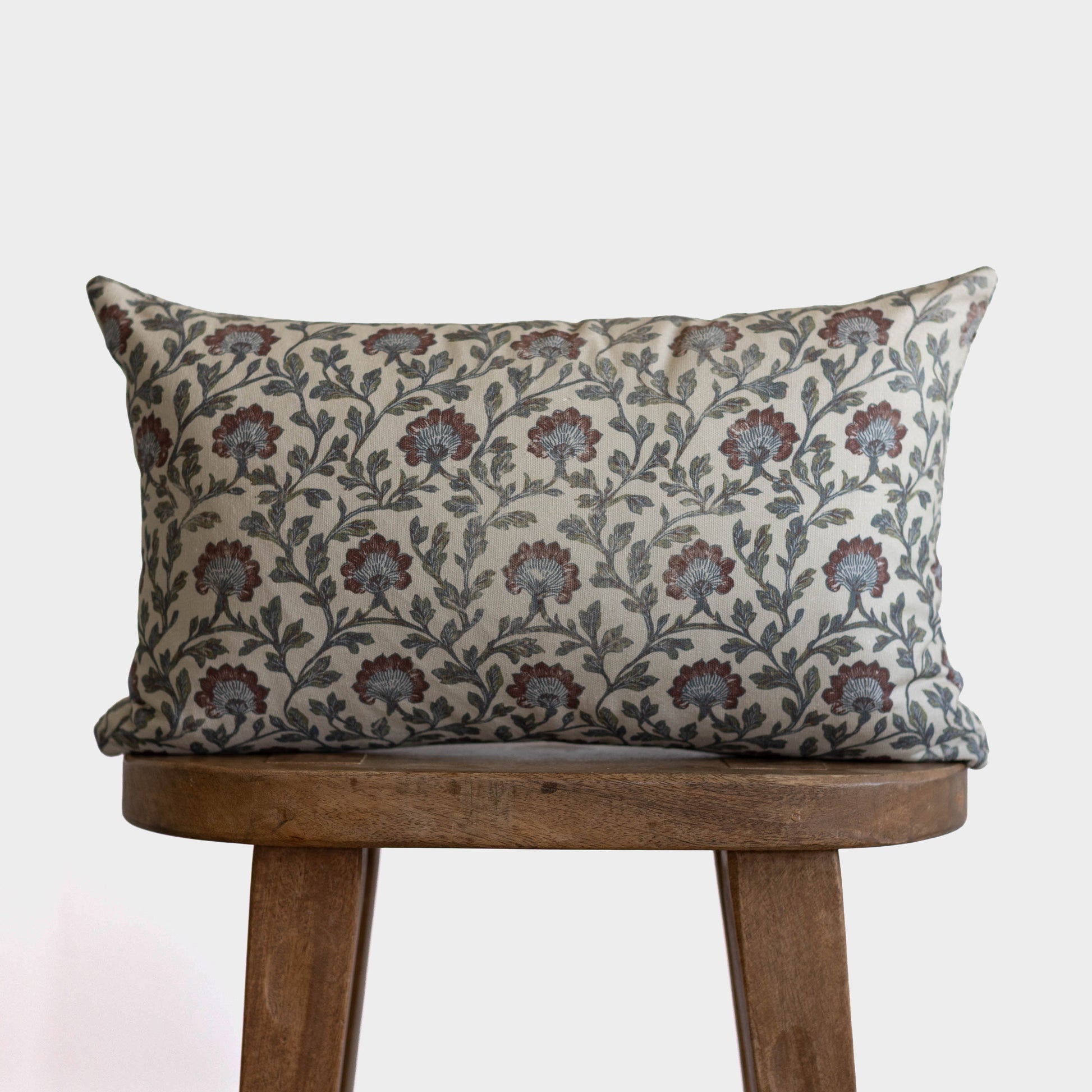 Rectangular pillow with cream background and burgundy and teal floral botanical print, displayed on wooden chair.