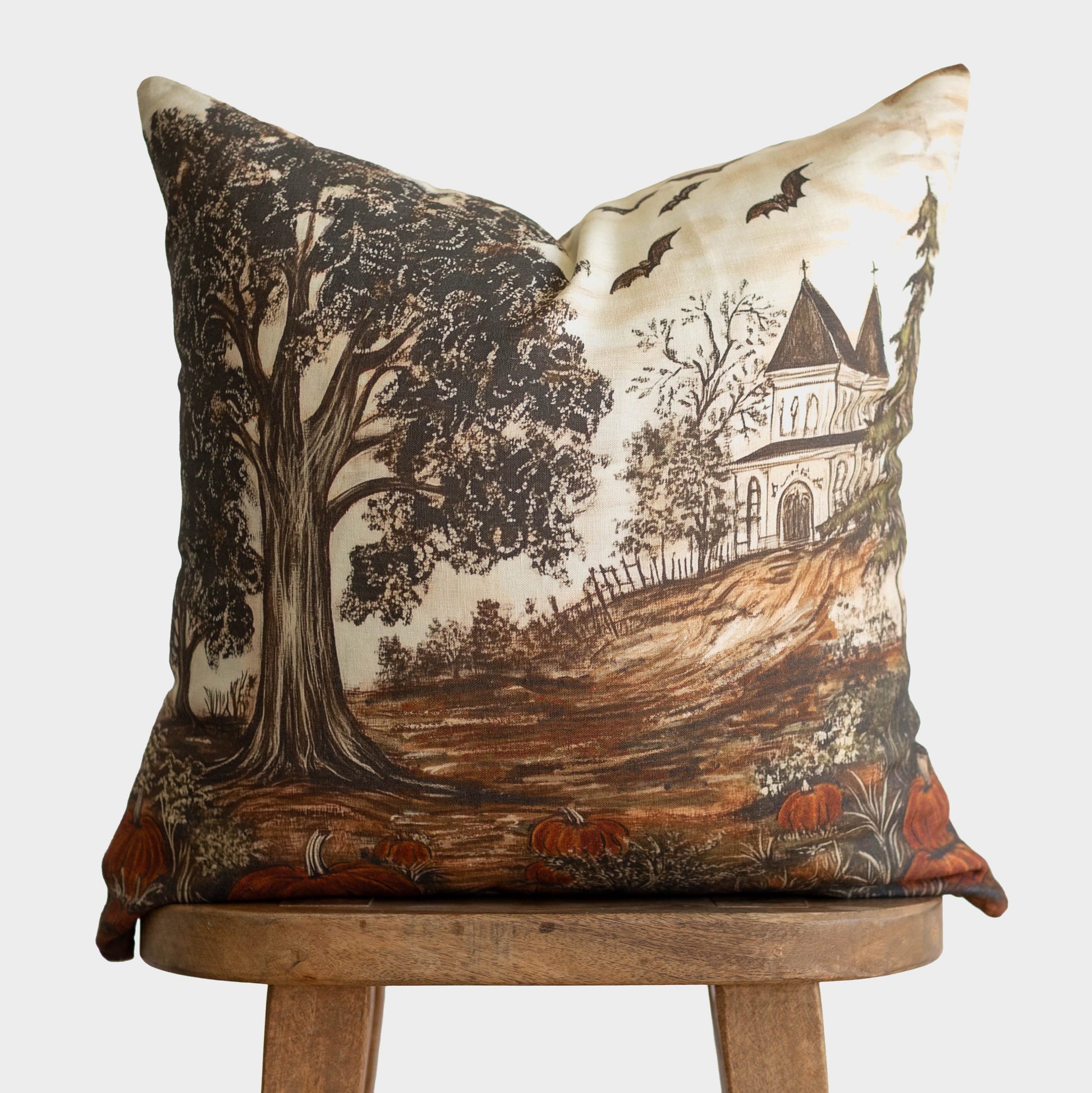 Linen pillow with illustration of gnarled tree, haunted house, bats, pumpkins, and bare branches in brown and cream tones.