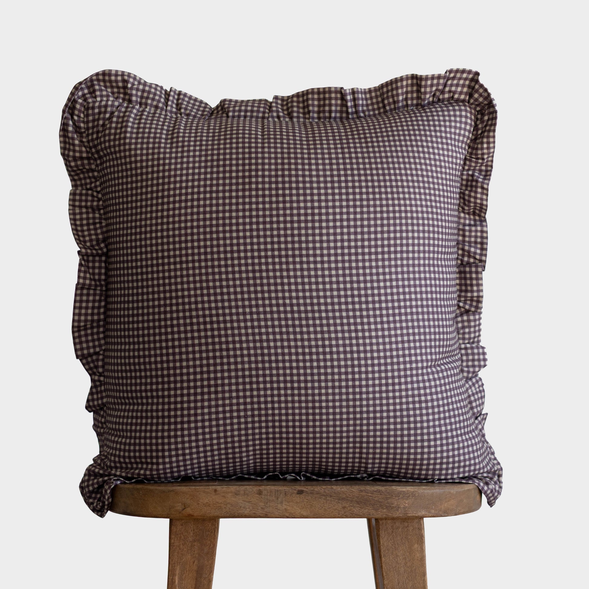 Plum gingham mini check pillow with ruffled edges on all sides, displayed on a wooden stool.
