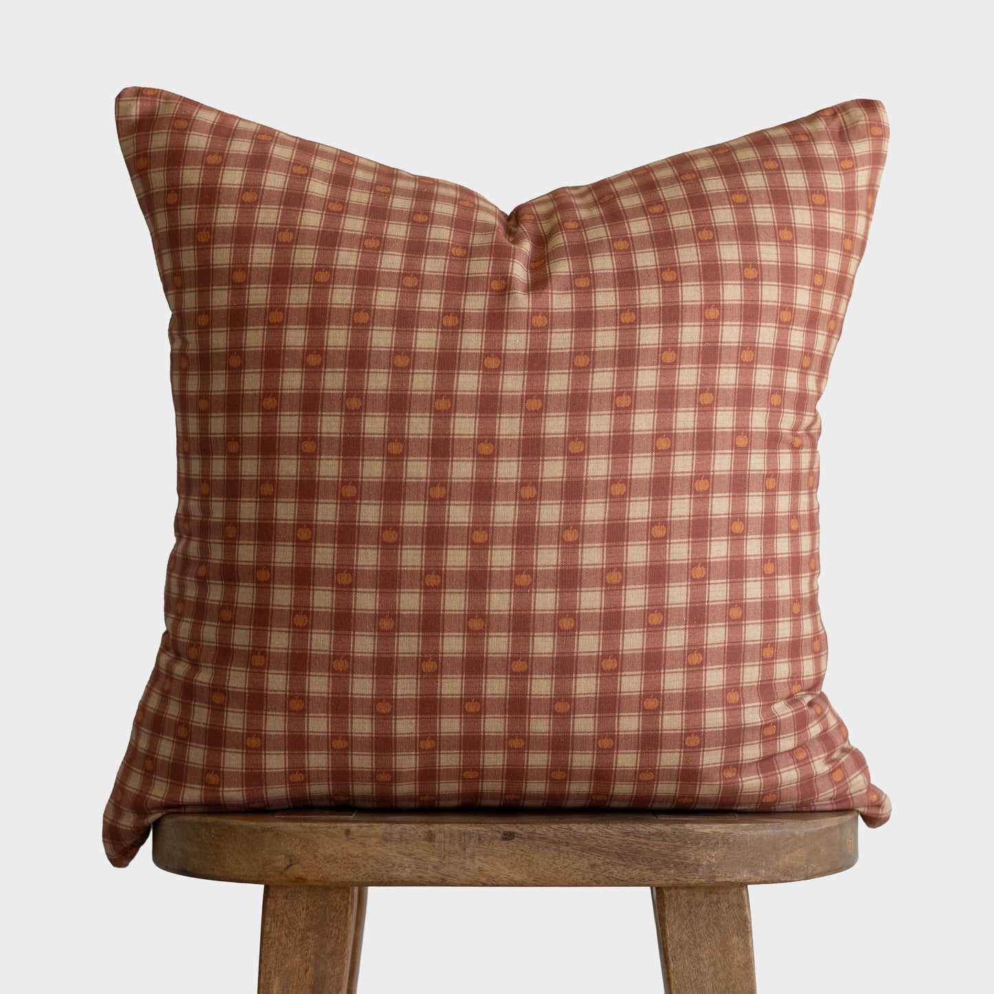 Red and cream plaid pillow with pumpkin-colored circular pattern details displayed on wooden stool.