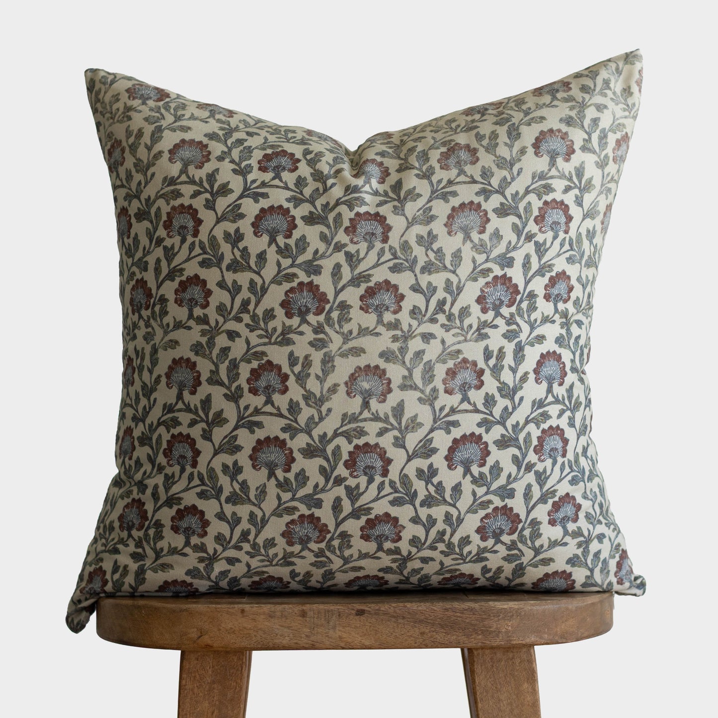 Clem pillow with multicolor floral and leaf pattern in burgundy, green, and cream on natural linen, displayed on wooden stool