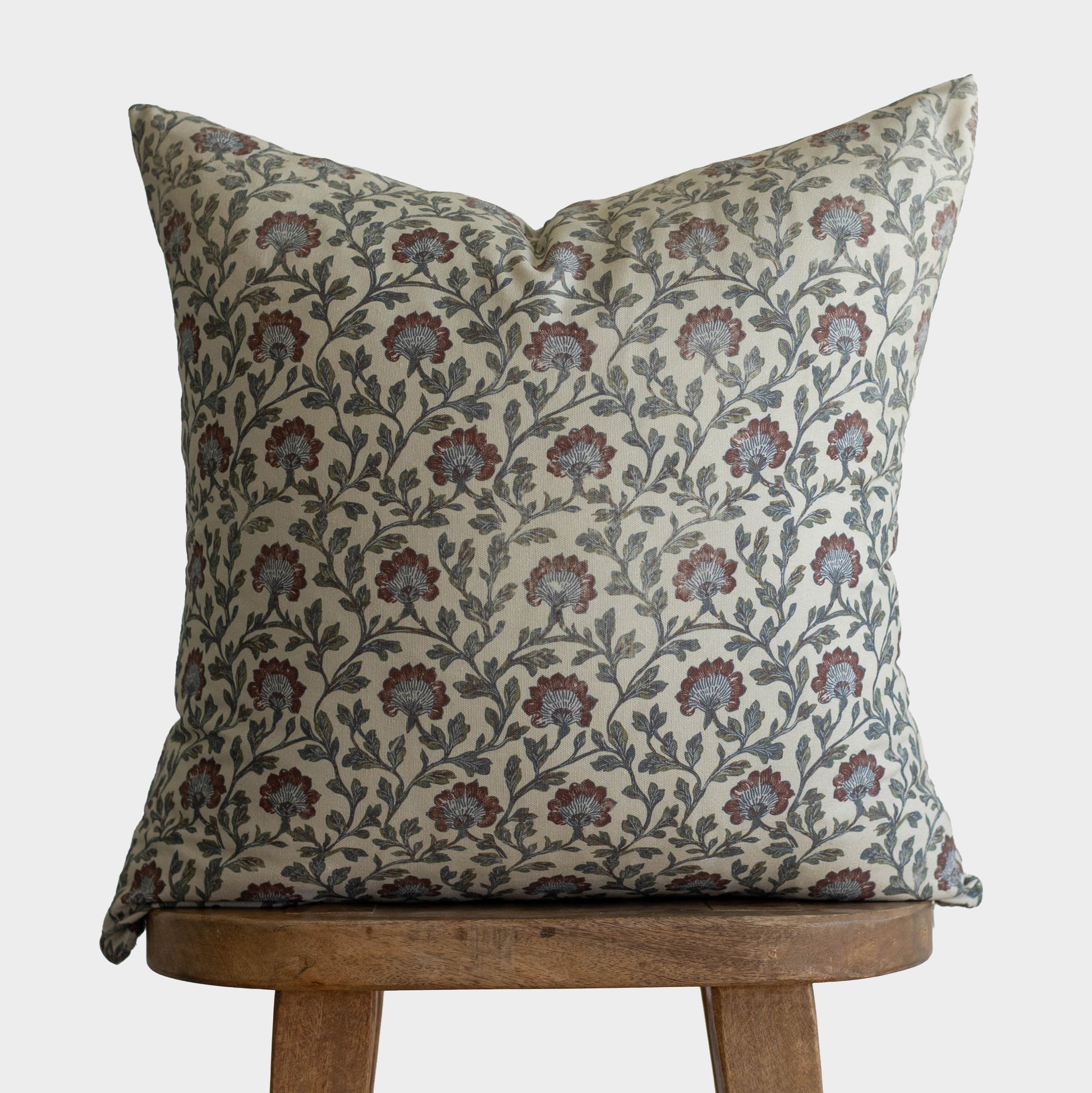 Clem pillow with multicolor floral and leaf pattern in burgundy, green, and cream on natural linen, displayed on wooden stool